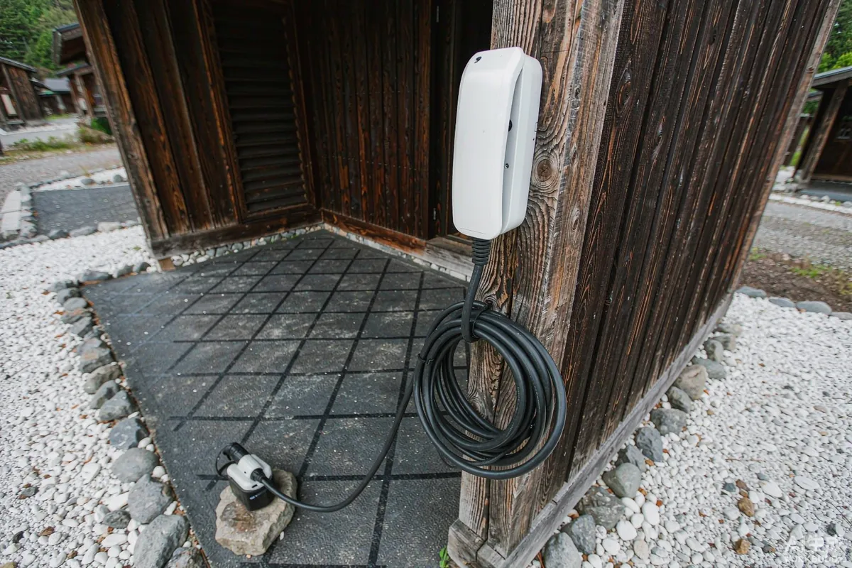 Close-up of a wall-mounted EV charging unit with coiled cable on a timber post at a capsule home parking space