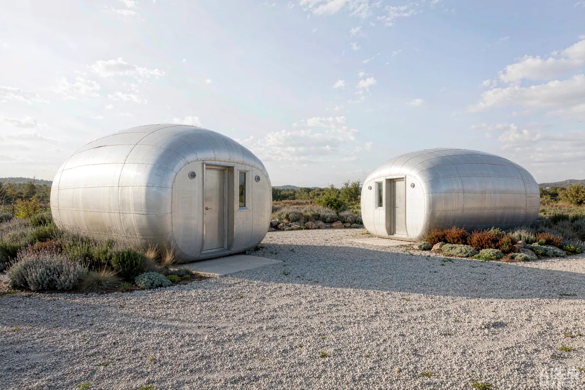 Two capsule homes spaced apart on a cleared gravel site with maintained defensible space
