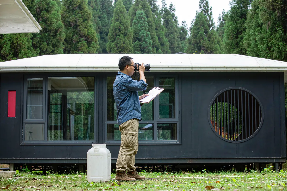Site manager photographing a window pane and noting strike details on a checklist near a capsule home