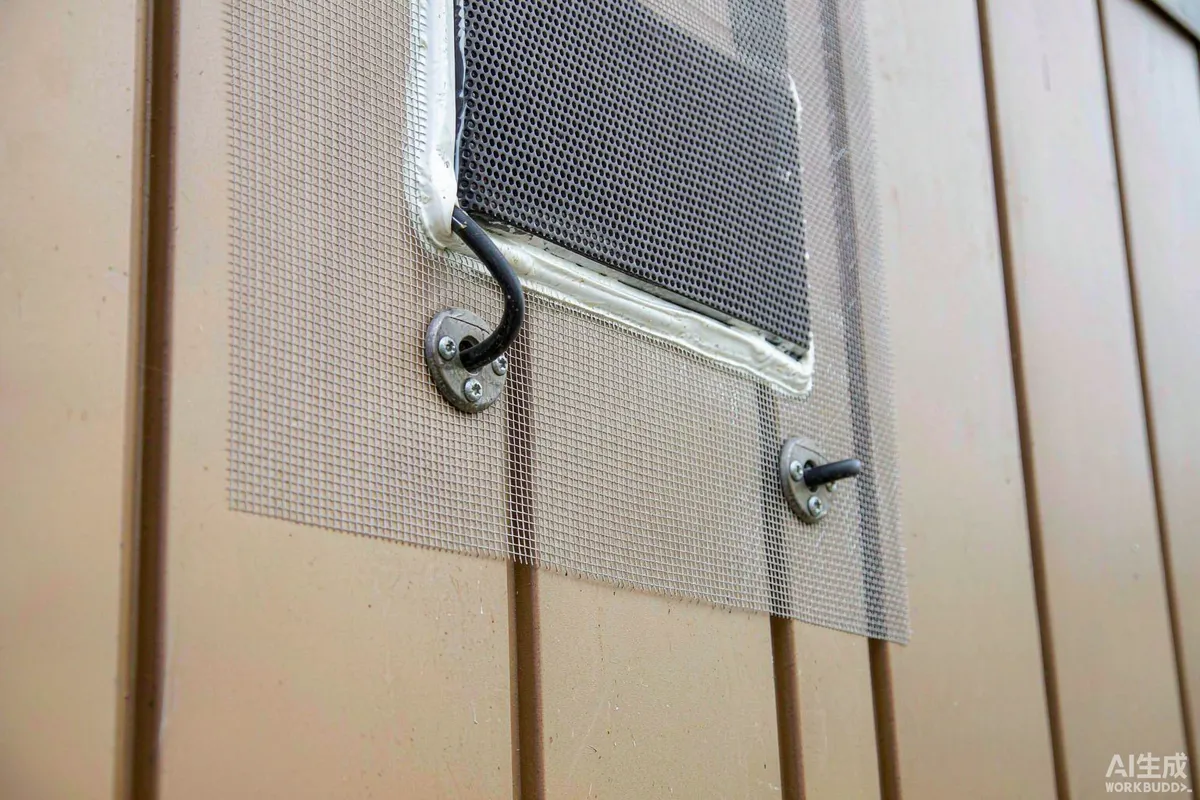 Close detail of fine stainless steel insect mesh over a ventilation grille and sealed cable entry on a capsule home exterior wall