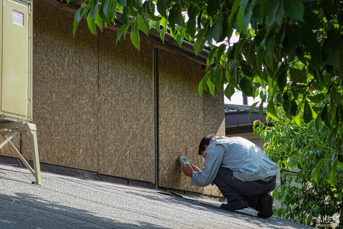 Technician checking an insulated wall panel seam on a prefab house exterior with a handheld gauge