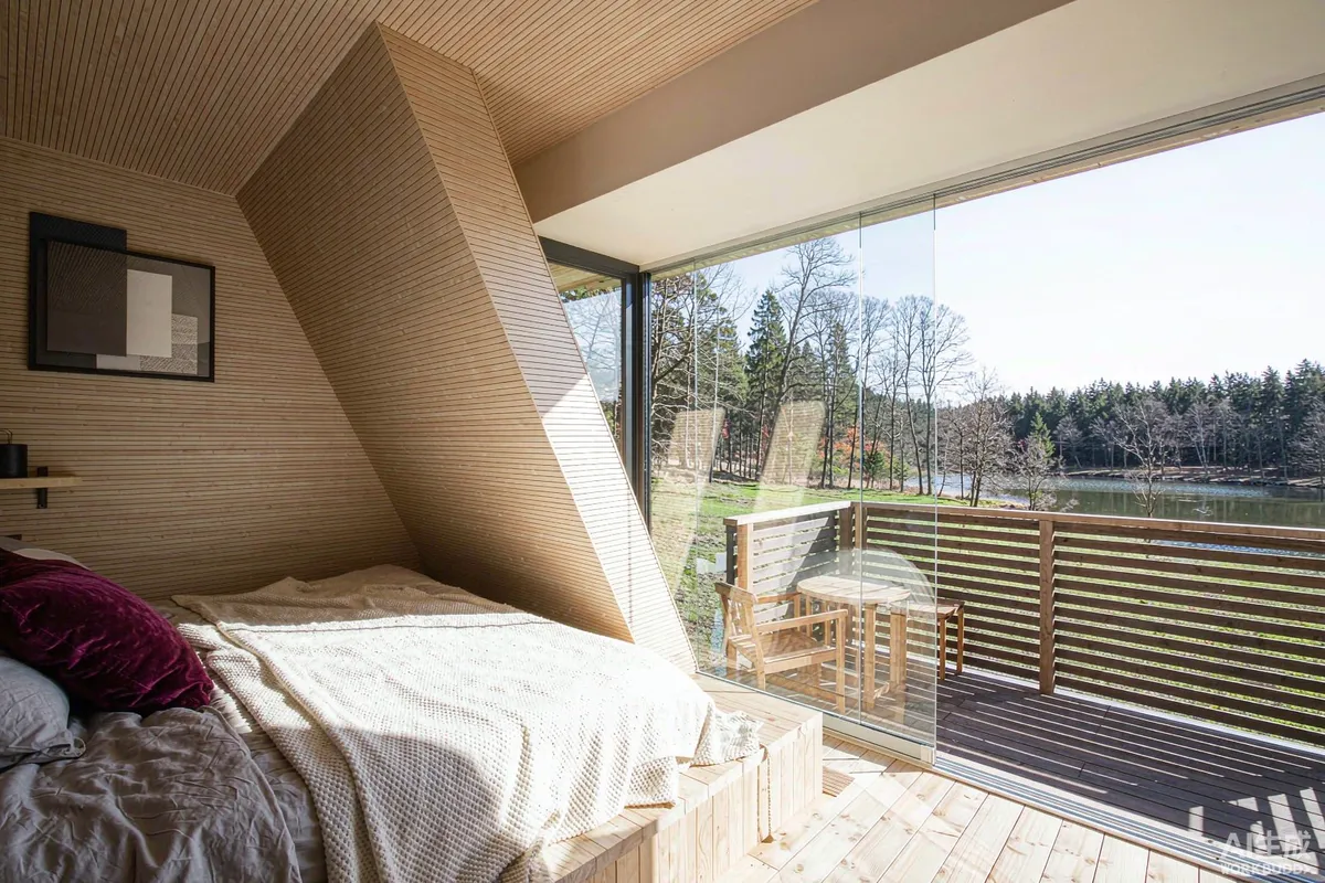 Prefab cabin interior with wood-lined walls, a bed and large glazing