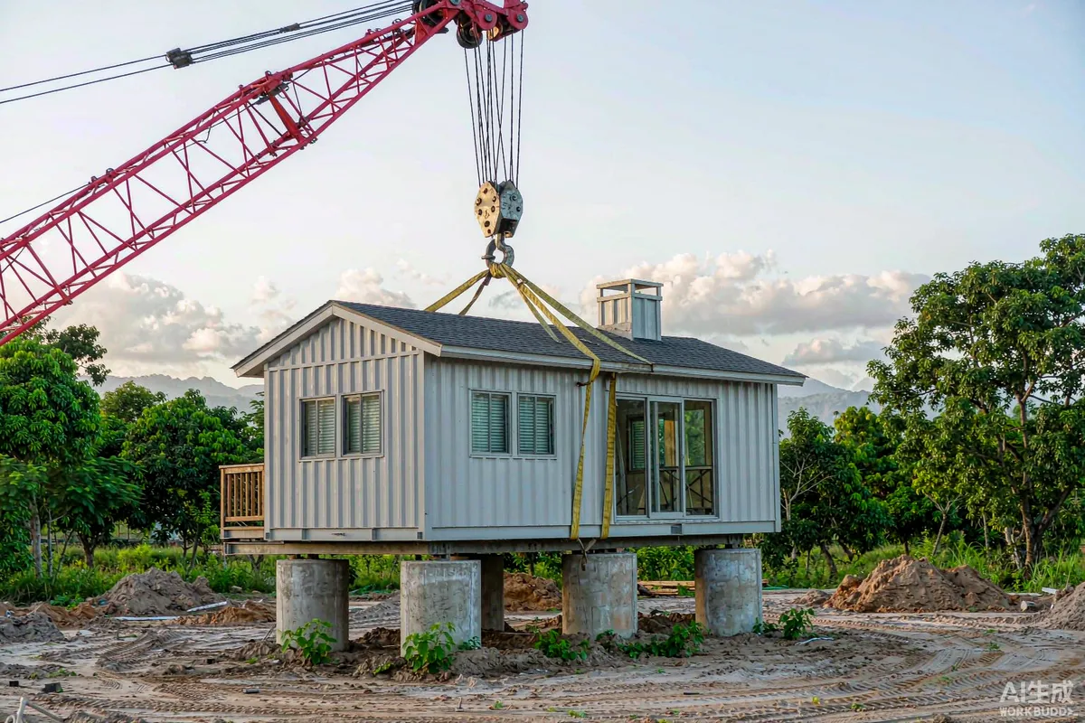 Crane lifting a finished modular dwelling onto prepared concrete piers on a tropical site